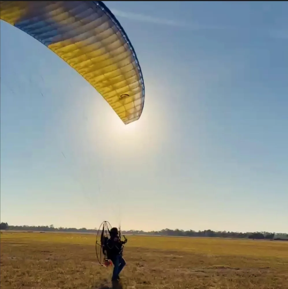 Launching a paramotor from an open field, the wing arcing overhead against the sun